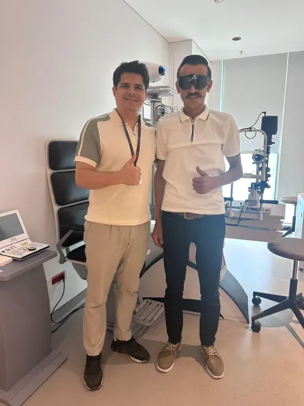 A patient after eye surgery, wearing protective glasses, beside his Eyeglow Health coordinator